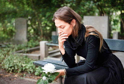 Uma mulher sentada com a mão apoiada no queixo, olhando para baixo com uma expressão de tristeza profunda, simbolizando o sofrimento e as dificuldades enfrentadas durante o luto.